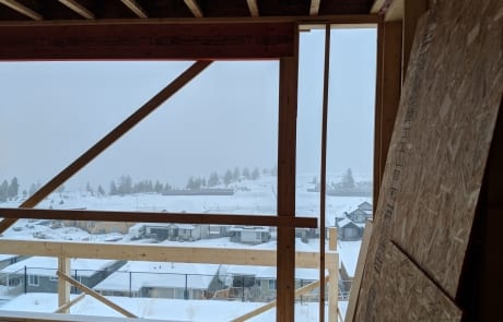 Construction site of custom home main floor during framing, view out of living room window in winter